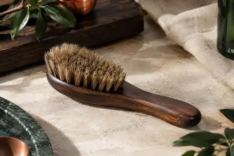 Brosse à barbe Cremo noire en sisal naturel et bois, posée sur une pierre claire.